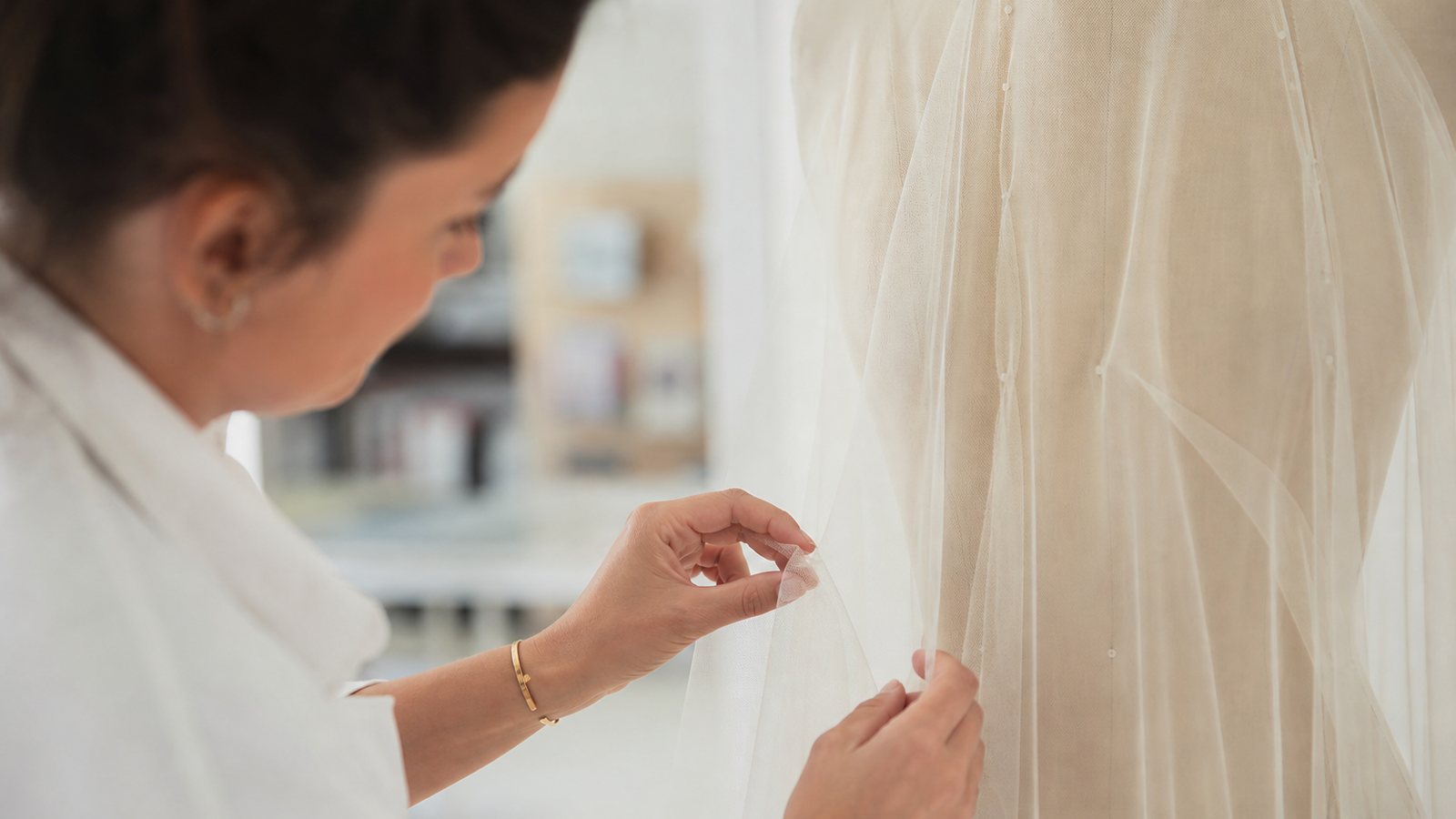 Voile de tulle de soie et bijou de tête posés près d'une robe de mariée à l'atelier