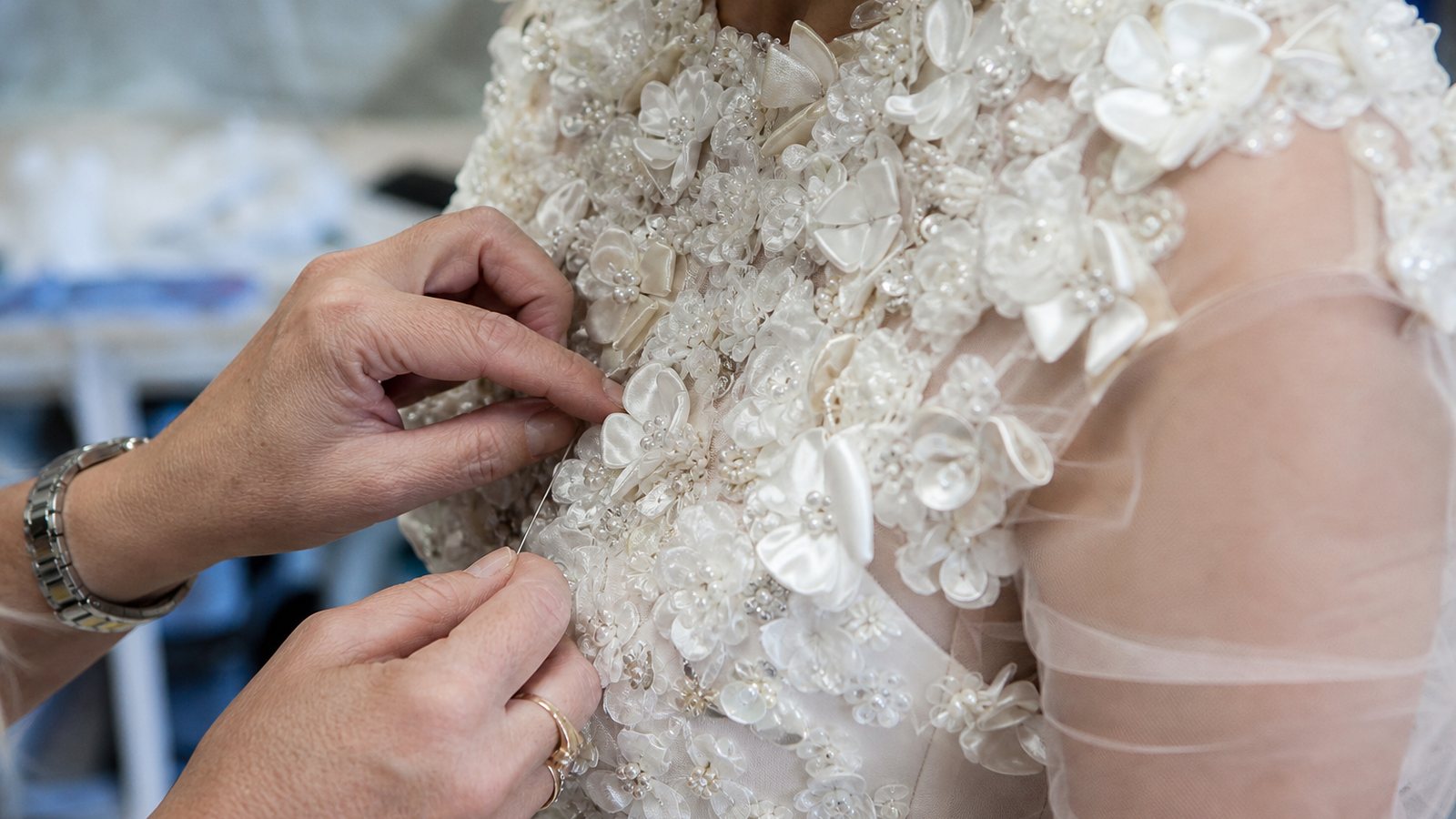 Mains d'une brodeuse cousant des perles a la main sur le corsage d'une robe de mariee