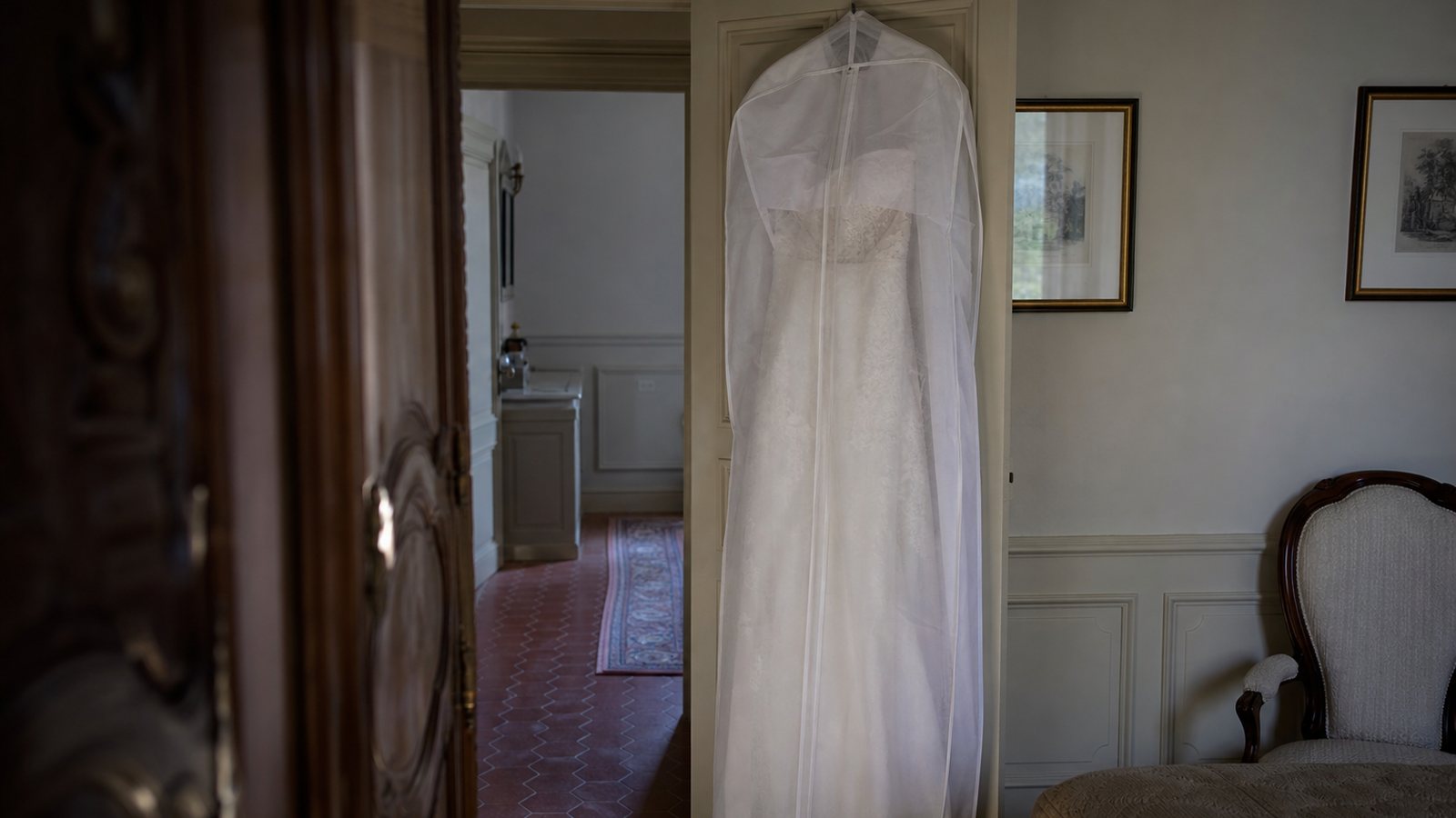 Robe de mariée protégée dans une housse en coton sur un cintre large avant le départ pour la cérémonie